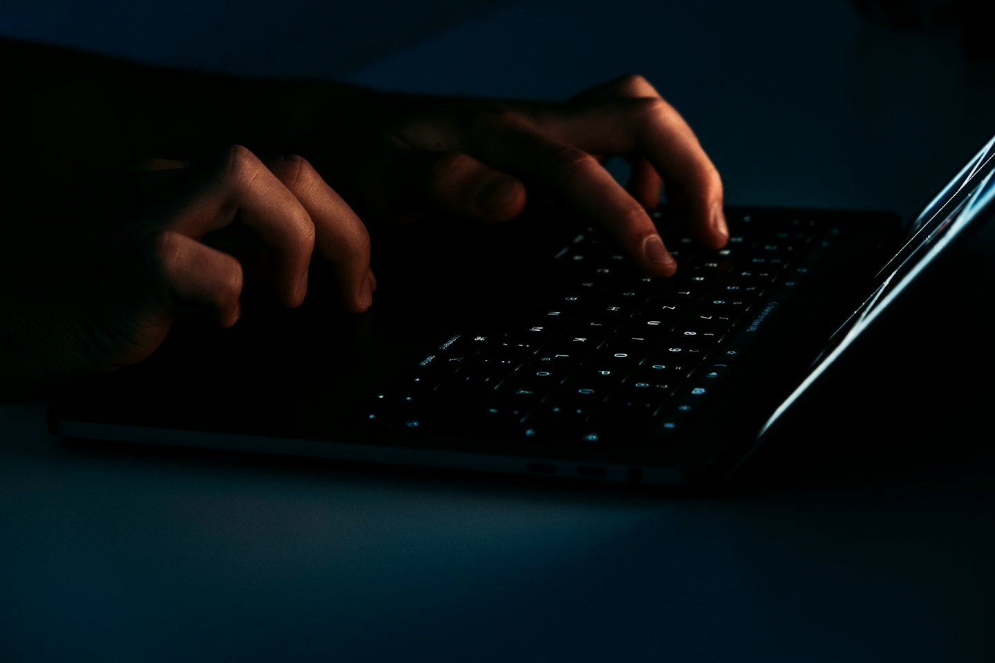 Mani che digitano su una tastiera luminosa di un laptop al buio.